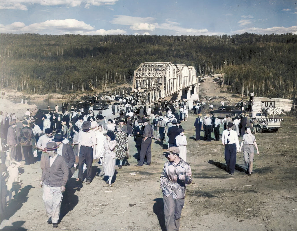 Colourized photograph taken in 1952 of a large group of people walking away from a bridge. A parade float on the back of a pickup truck is in the background and there are cars parked on the approach to the bridge.