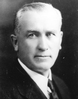 Black and white portrait photograph of a middle-aged man wearing an suit and tie.